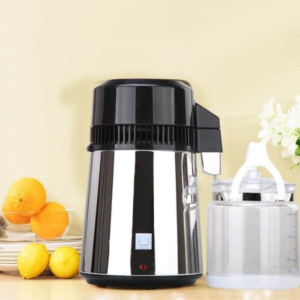 Stainless steel citrus juicer with black lid situated on a kitchen counter alongside fresh lemons and oranges.